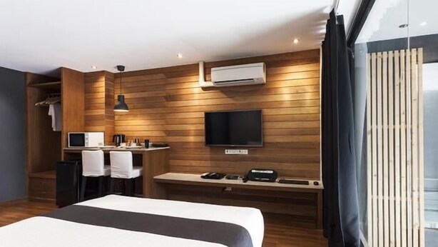 A modern hotel room with a large bed, a desk with a chair, a flat-screen TV, and an air conditioning unit. - 5ive Beach House Hotel (Pattaya)