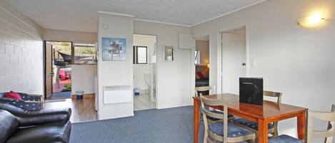 A compact living space with a dining area, a sofa, and a kitchen visible through an open door.