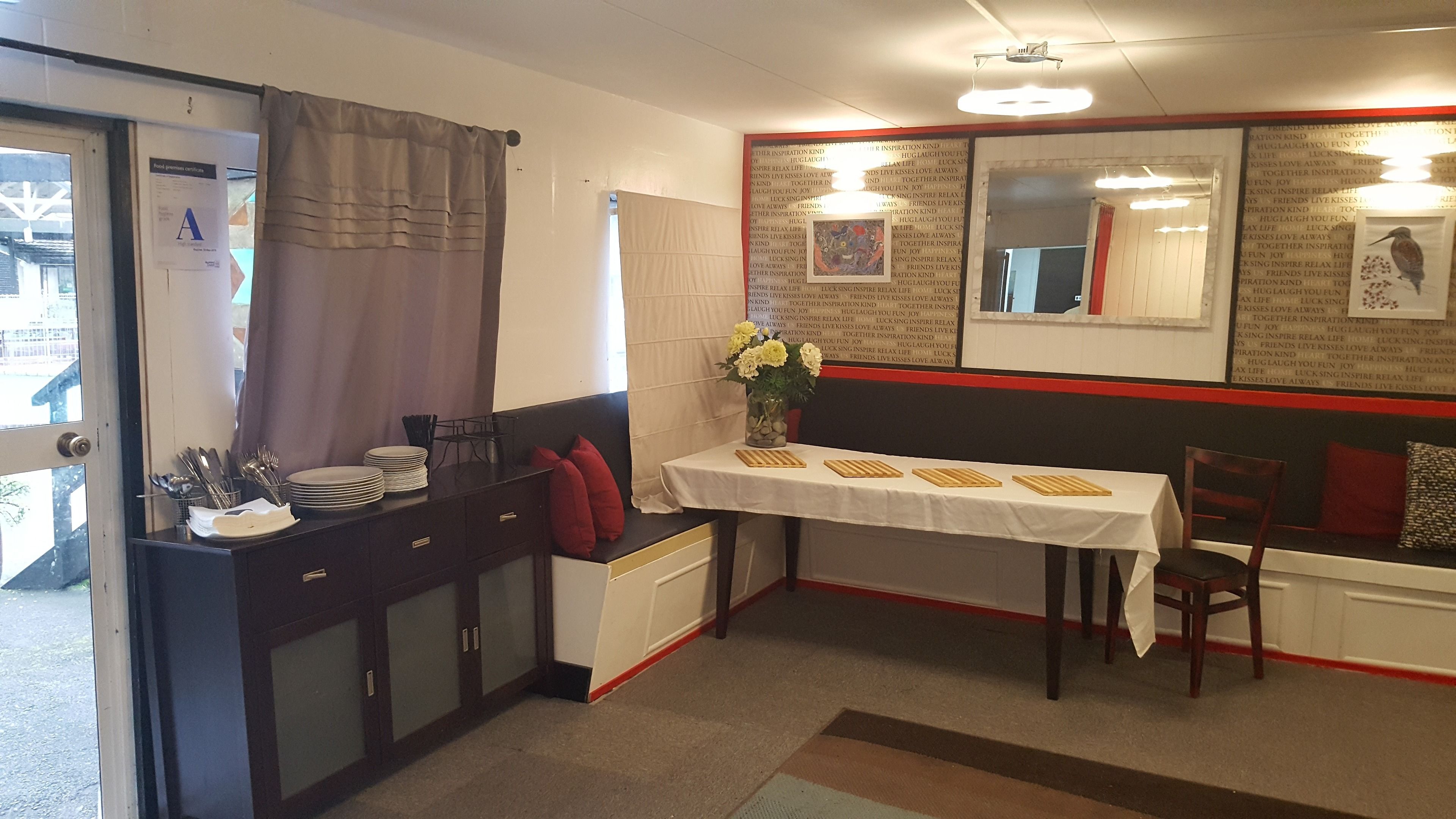 Cocina compacta con comedor, que incluye una mesa para dos personas, un armario con utensilios y una ventana con cortinas.