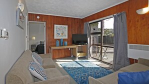Un espacio habitable compacto con un sofá, televisión, escritorio y un ventanal grande.