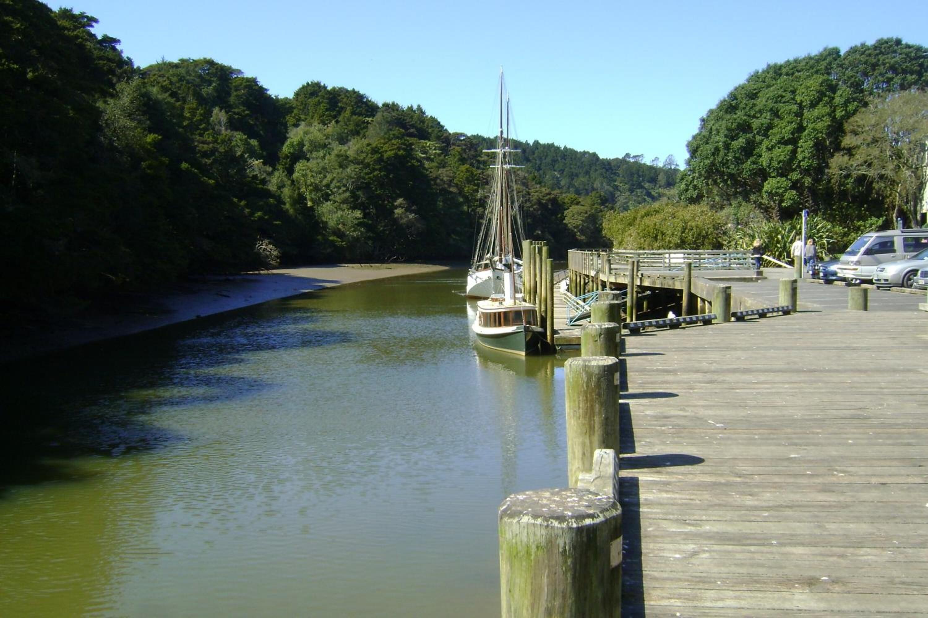 Un muelle de madera se extiende sobre un río tranquilo, con un velero amarrado al final.
