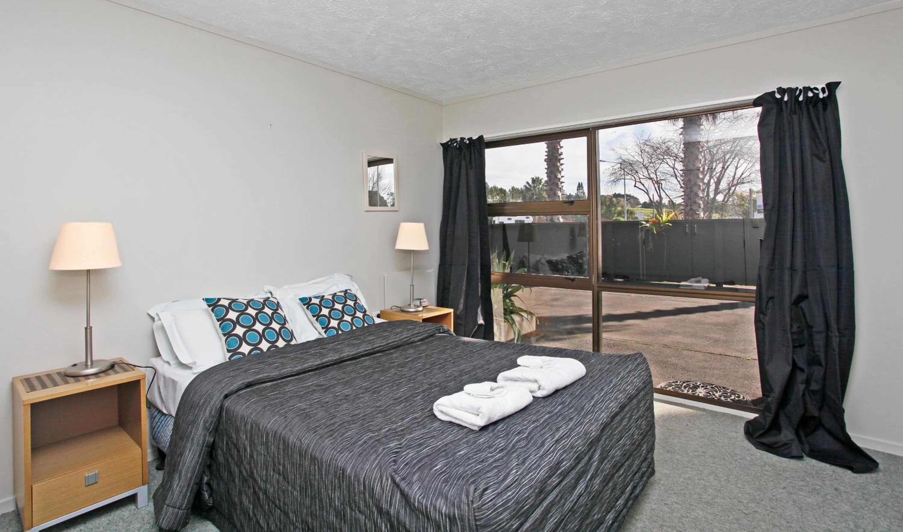 A bedroom with a large bed, two bedside tables, a window with curtains, and a view of the outside.