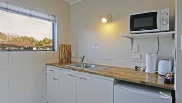 Una kitchenette con un fregadero, un microondas, una tabla de cortar de madera y una ventana que ofrece vistas a edificios.