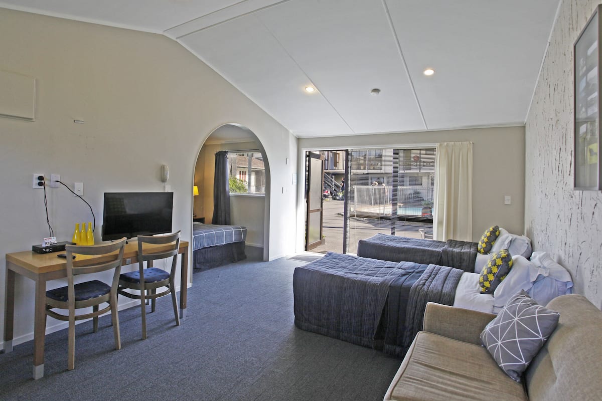 A hotel room with a desk, two chairs, a bed, and a TV.