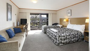 Habitación de hotel con sofá, dos camas, televisión, escritorio y balcón con vistas.