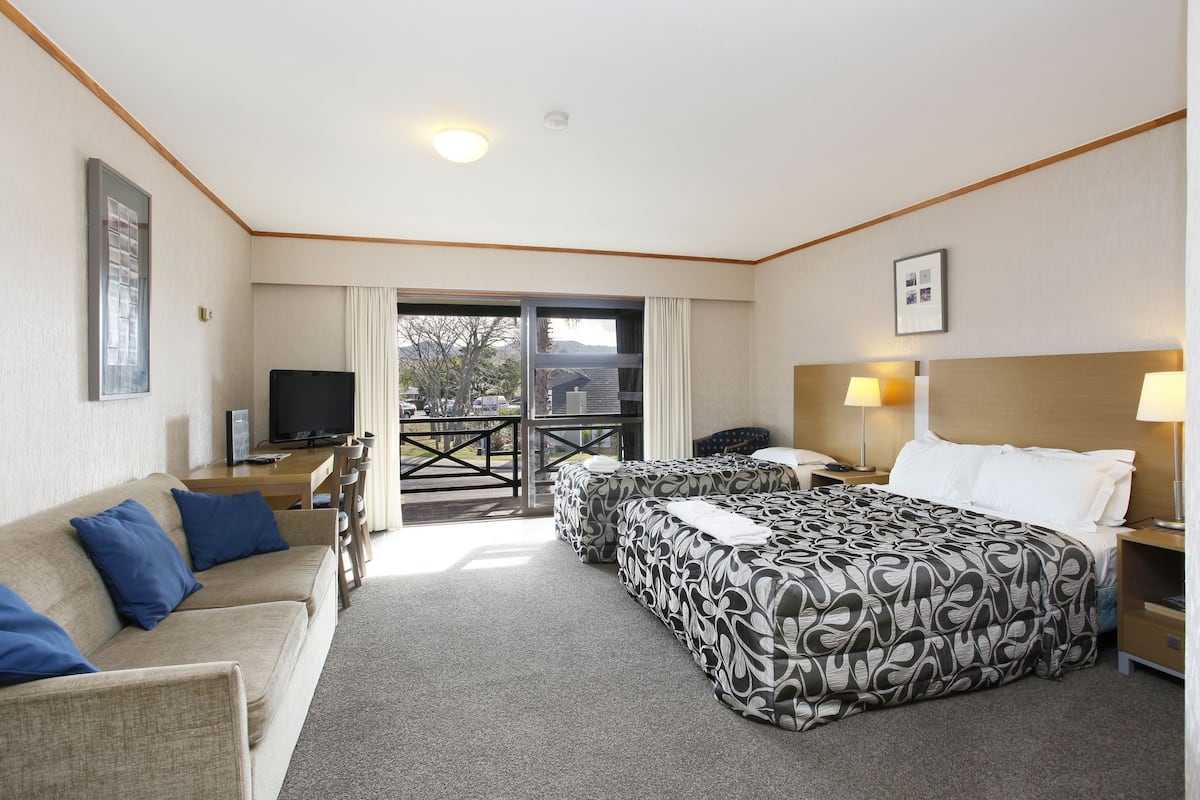 A hotel room with a sofa, two beds, a TV, a desk, and a balcony with a view.