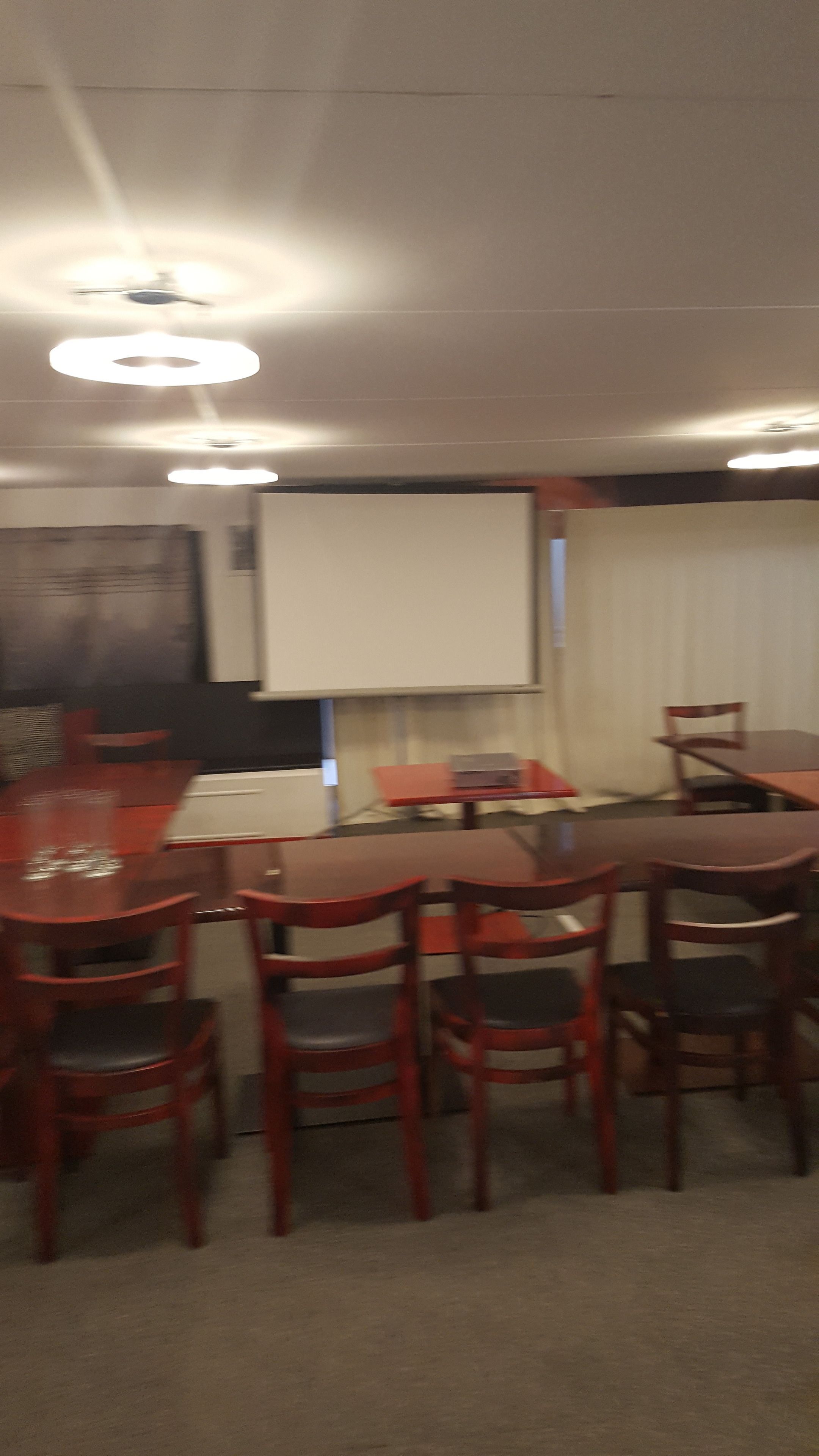 Un salón de conferencias con una gran mesa y sillas, una pantalla de proyector y luces en el techo.