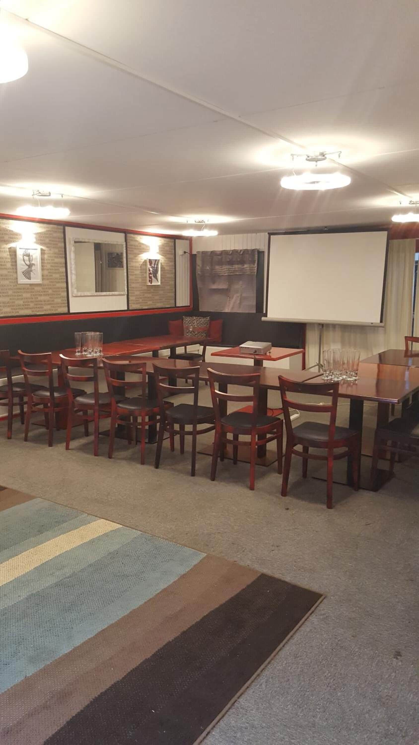 A conference room with a projector screen, wooden tables, and chairs.