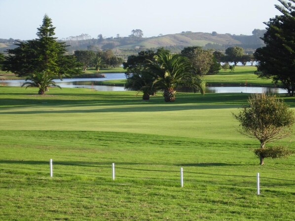 Un campo de golf con un cuerpo de agua, árboles y un paisaje montañoso al fondo.