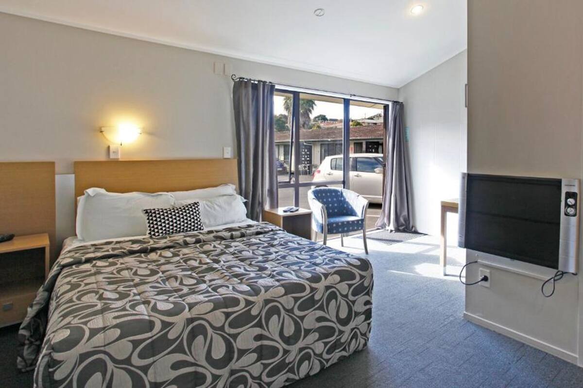 A hotel room with a large bed, a TV, a chair, and a view of the outside.