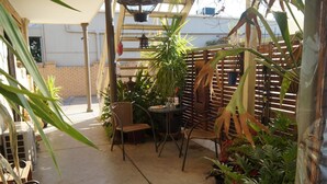 Un patio couvert avec une table et des chaises, entouré de plantes en pot et d’une clôture en bois.