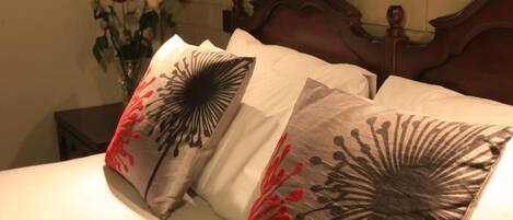 A bed with two pillows featuring a black and red floral design, a wooden headboard, and a vase with flowers on a bedside table.
