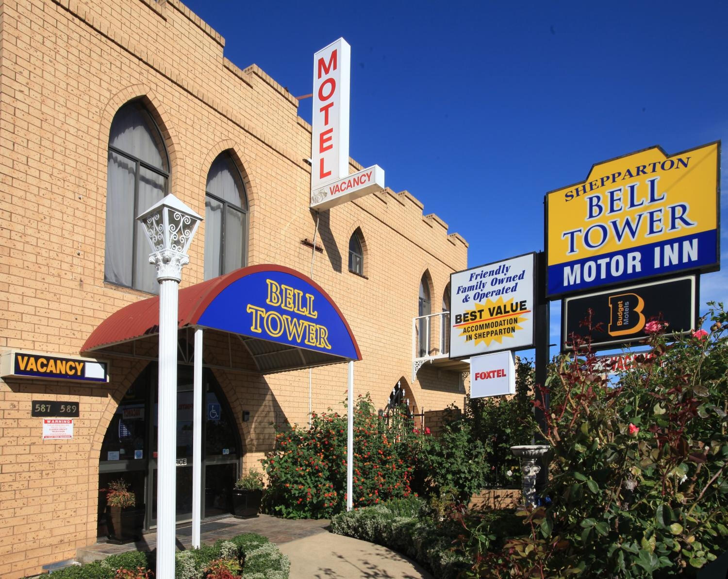 Un motel avec une enseigne représentant une « tour avec cloche », une autre simplement indiquant « Motel » et une troisième, plus complète, indiquant « Bell Tower Motor Inn ».