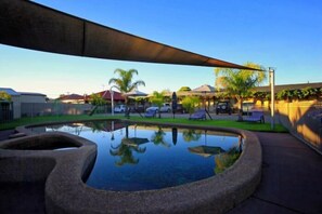 A swimming pool with a stone edge, surrounded by a shaded area and a fence.