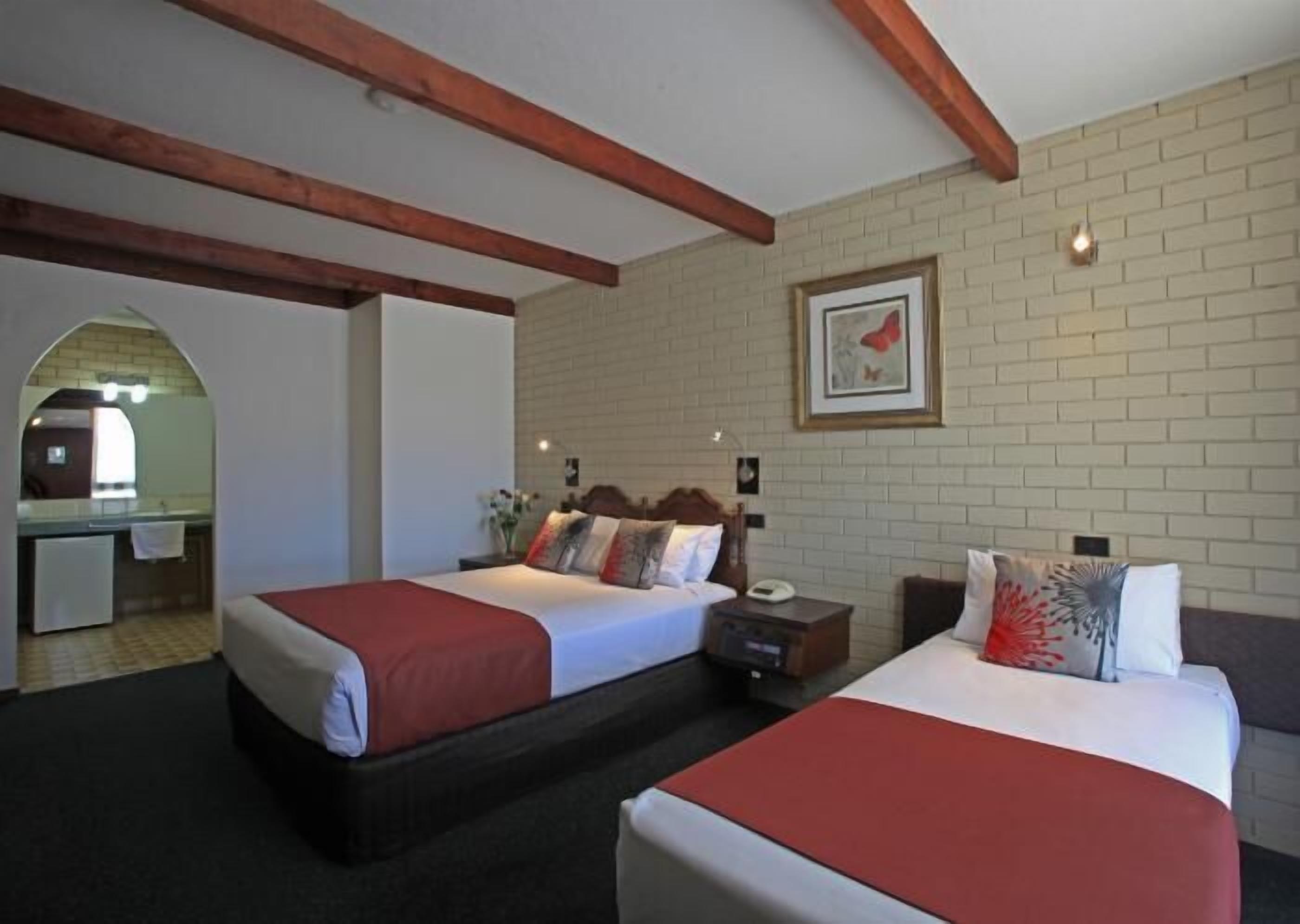 Een hotelkamer met twee bedden, een klein bureau en een bakstenen muur.