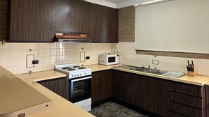 Une cuisine moderne avec des meubles de couleur bois foncé, un plan de travail blanc, un four encastré et un four à micro-ondes.