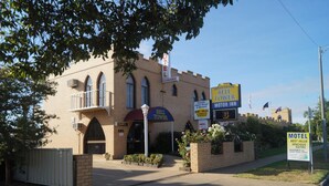Un motel avec une enseigne indiquant qu’il s’agit d’un « Bell Tower Motor Inn », caractérisé par une façade en briques, des fenêtres en arc de cercle et un petit balcon.
