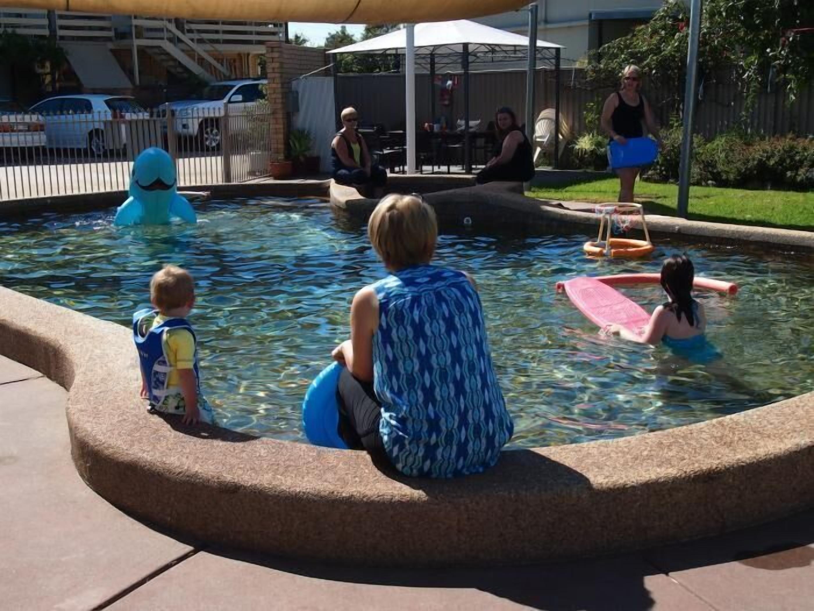 A pool area with a paved walkway and a covered seating area.
