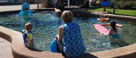 A pool area with a paved walkway and a covered seating area.