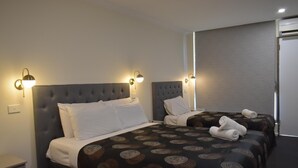 Une chambre d’hôtel avec deux lits, chacun recouvert d’une couvre-lit à motifs foncés et agrémenté d’oreillers blancs. Des appliques murales sont fixées de part et d’autre des lits.