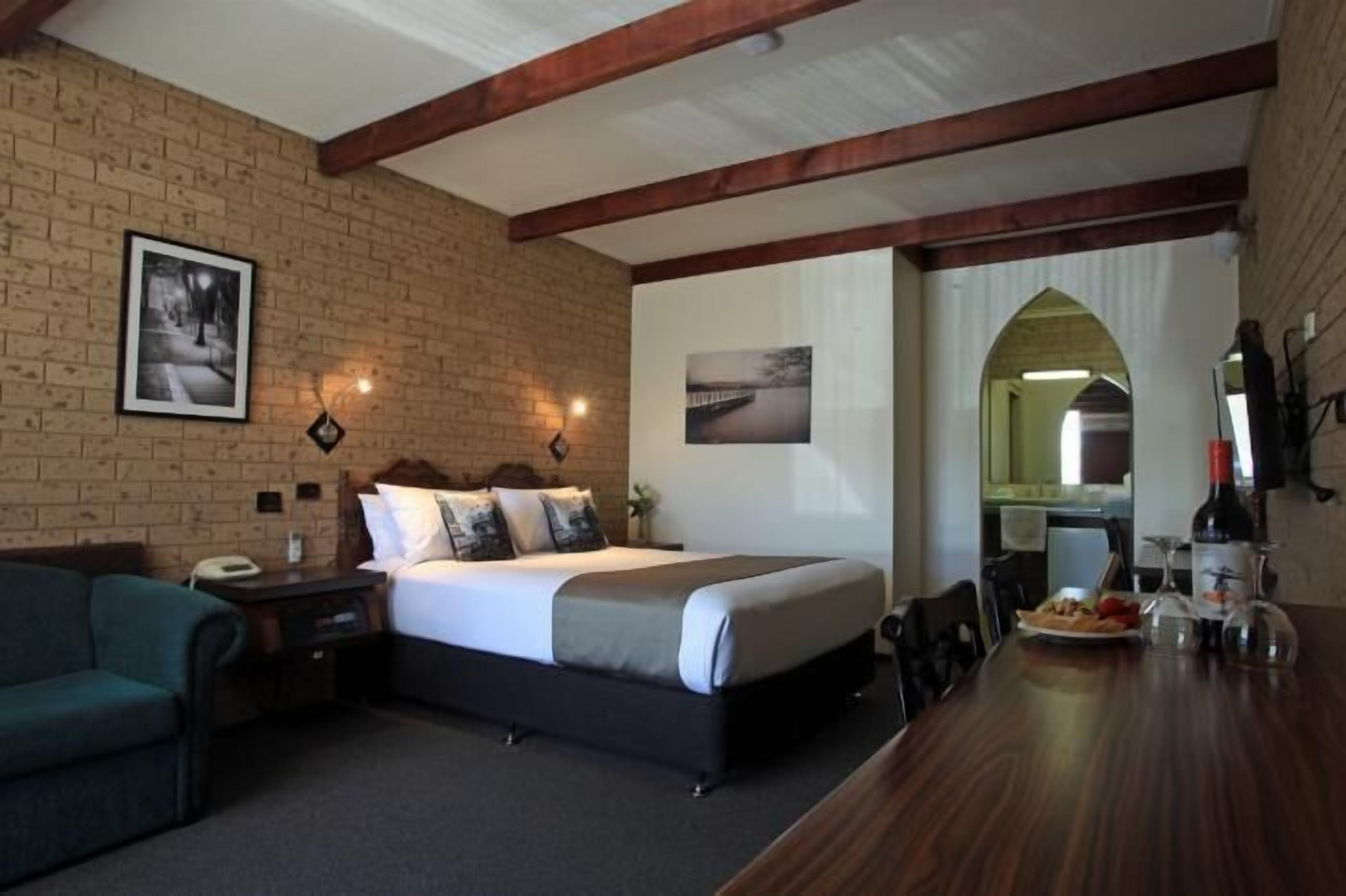 Una habitación de hotel con pared de ladrillo, una cama con cabecero, una mesa de madera con un plato de comida y un espejo.