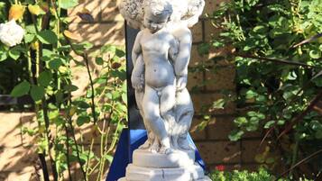 A stone fountain with a cherub statue, surrounded by greenery and a brick wall.