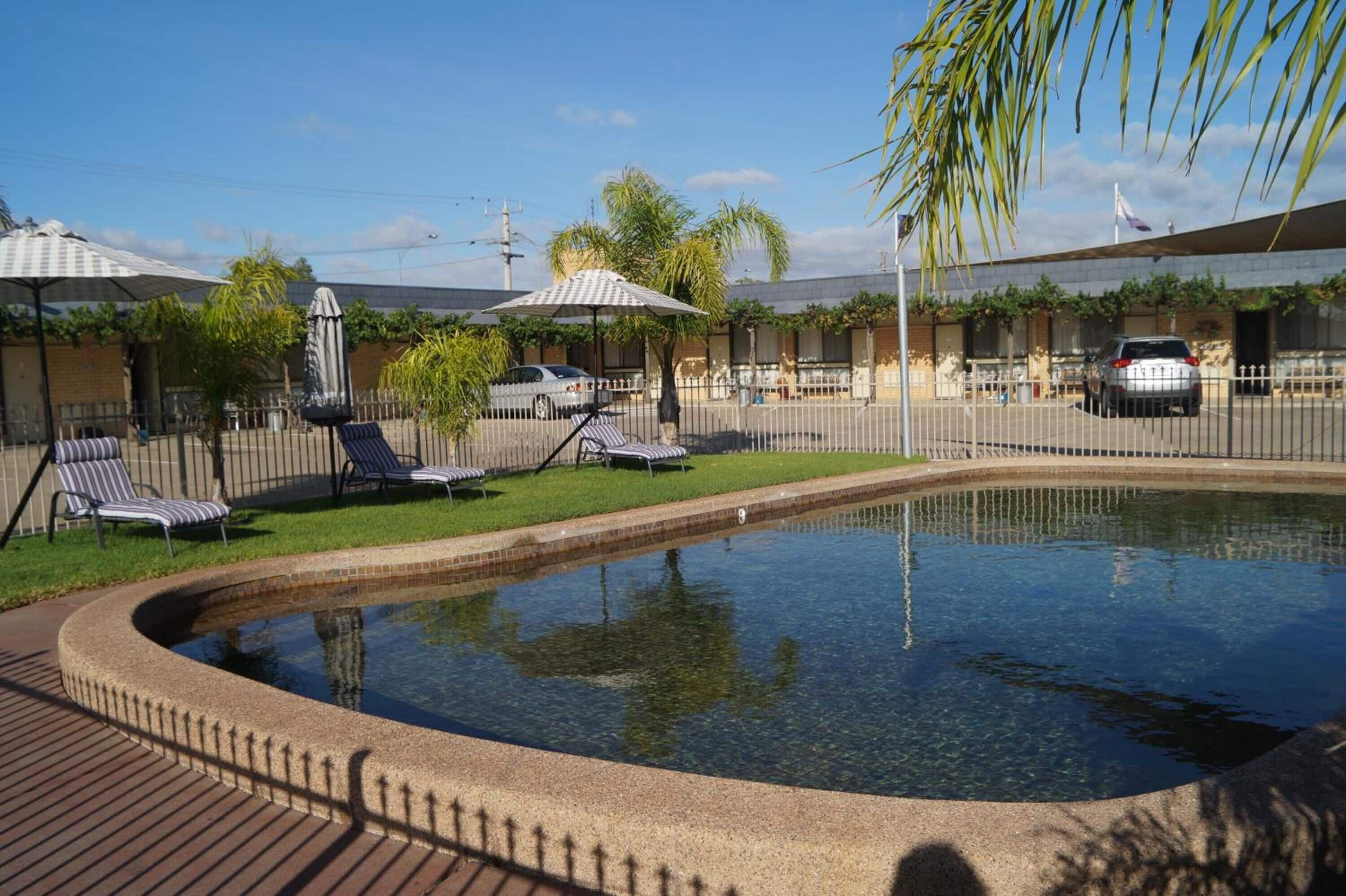 Une piscine entourée d’une clôture et de verdure, avec des chaises longues et des parasols.