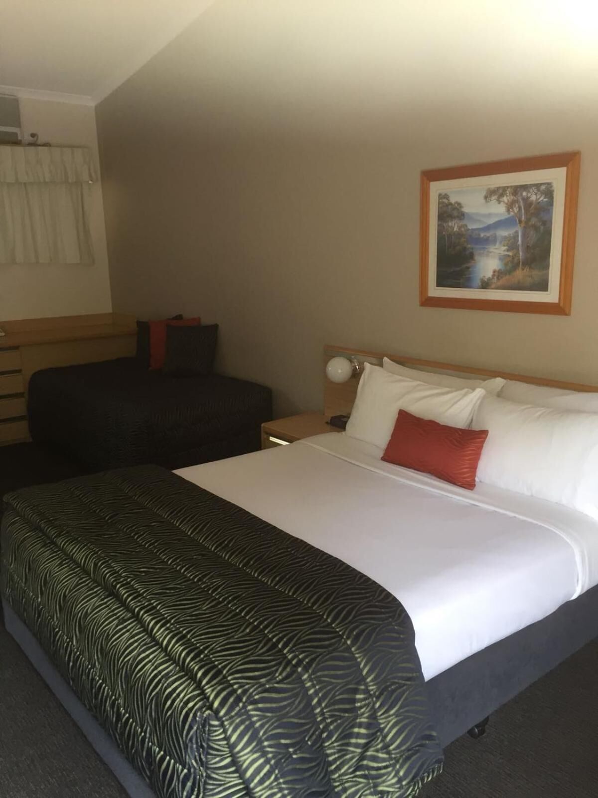 A hotel room with a large bed, a nightstand, a desk, and a painting on the wall.