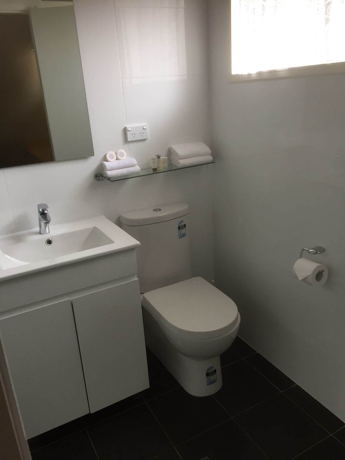 Un baño con lavamanos blanco, inodoro y estante con artículos de aseo.
