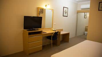 A hotel room with a wooden desk, a chair, a television, a bed, and a mirror.
