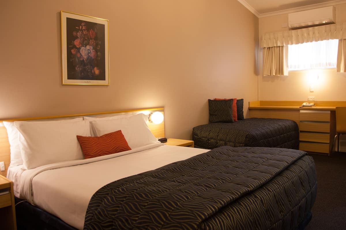 A hotel room with a large bed, a smaller bed, a desk, and a painting on the wall.
