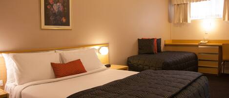 A hotel room with a large bed, a smaller bed, a desk, and a painting on the wall.