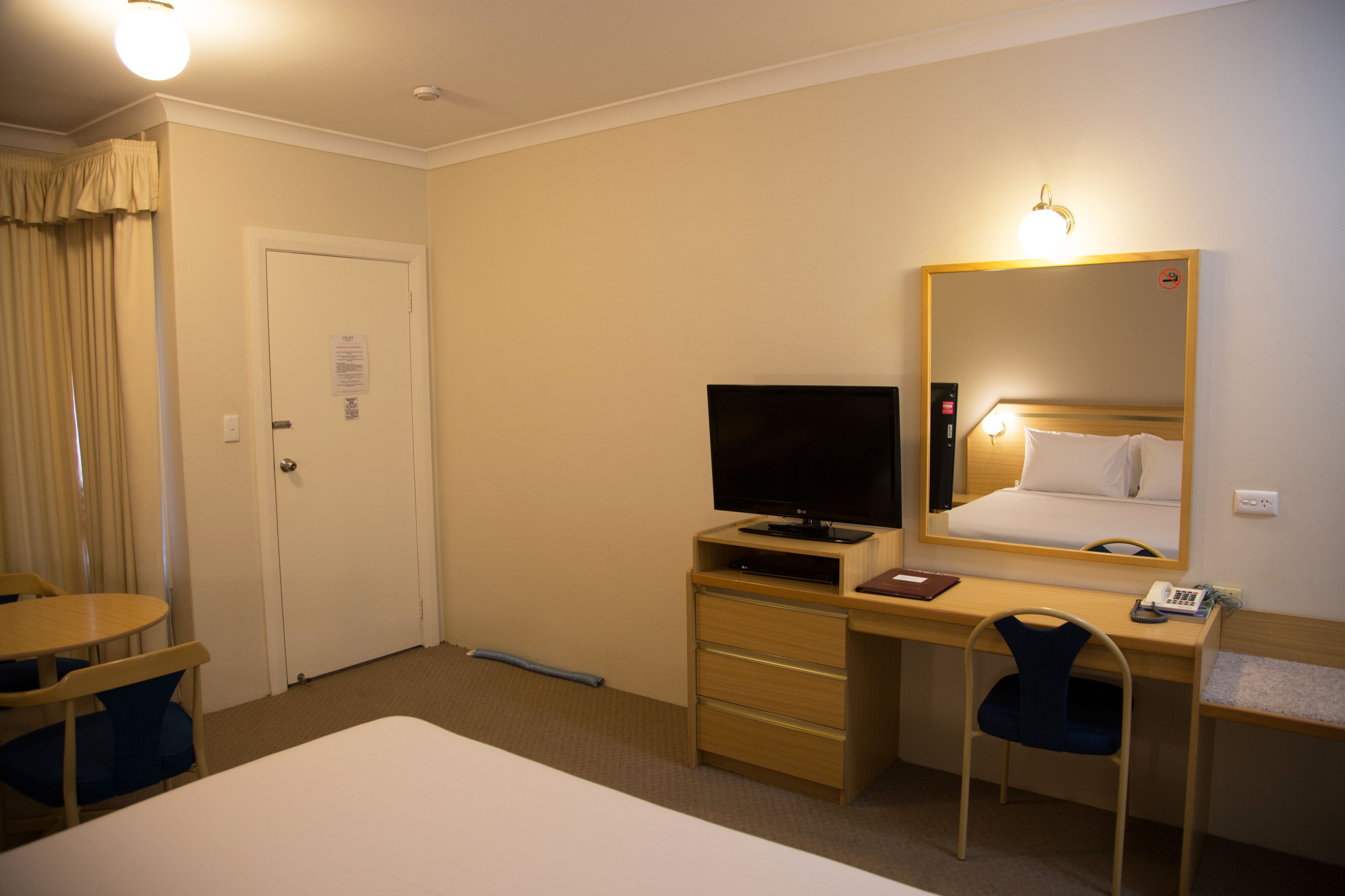 Habitación de hotel con una cama, un escritorio con ordenador, una silla, un televisor y un espejo.