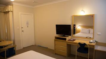 Habitación de hotel con una cama, un escritorio con ordenador, una silla, un televisor y un espejo.