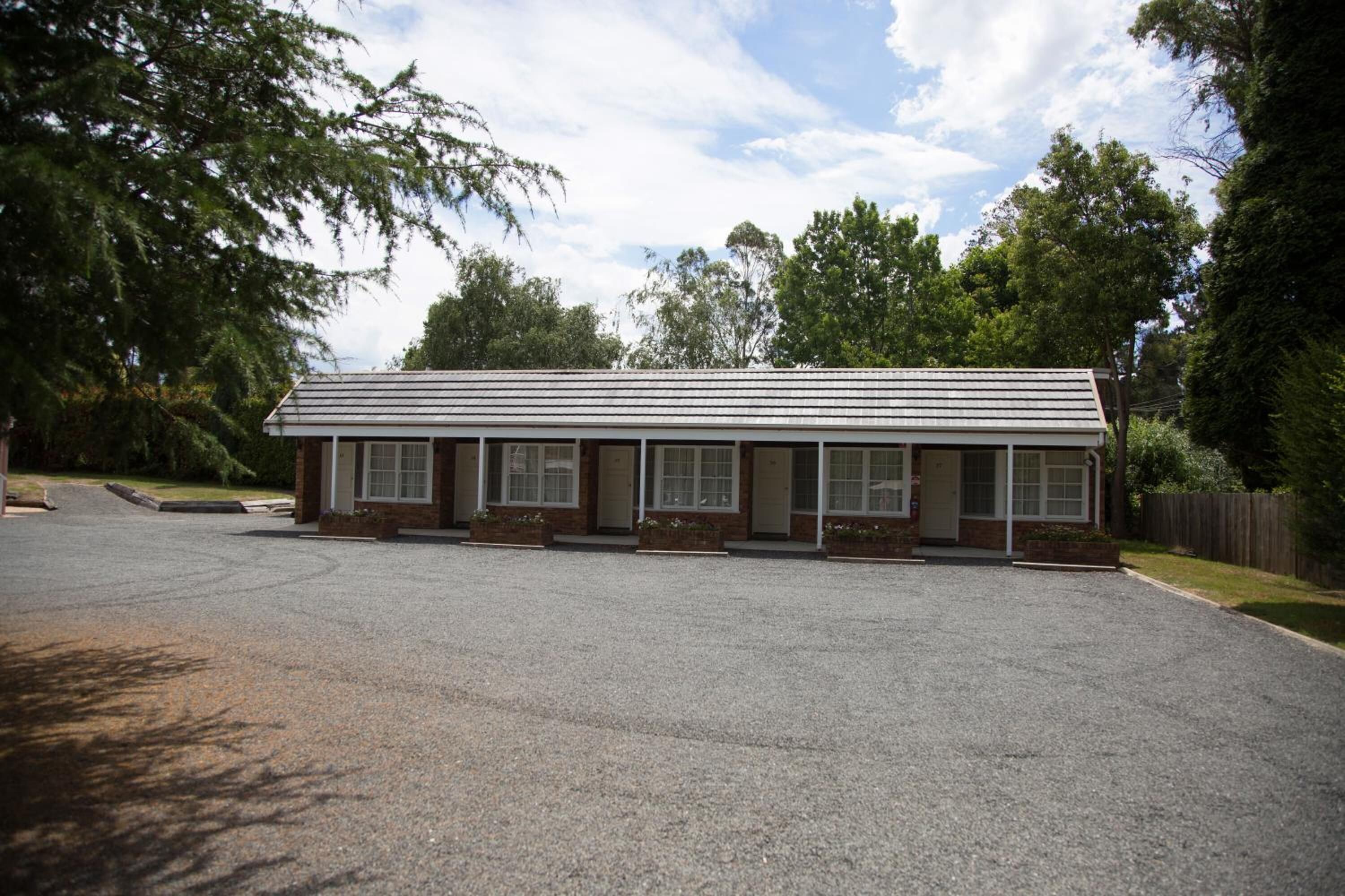 A single-story building with a flat roof, a front porch with a bench, and a driveway leading to the entrance.