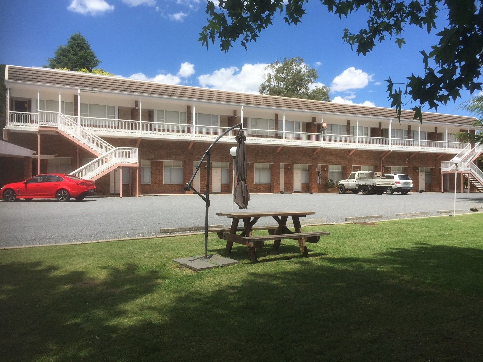 A motel with a two-story structure, a covered parking area, and a picnic table in the foreground.