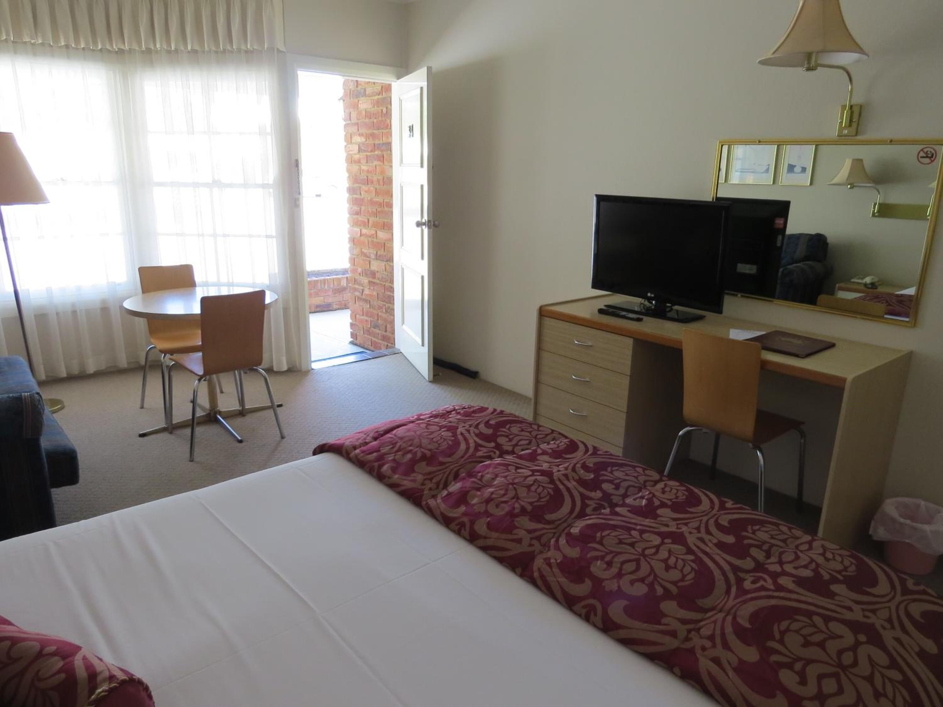 A hotel room with a bed, a desk with a television, a chair, and a window with curtains.