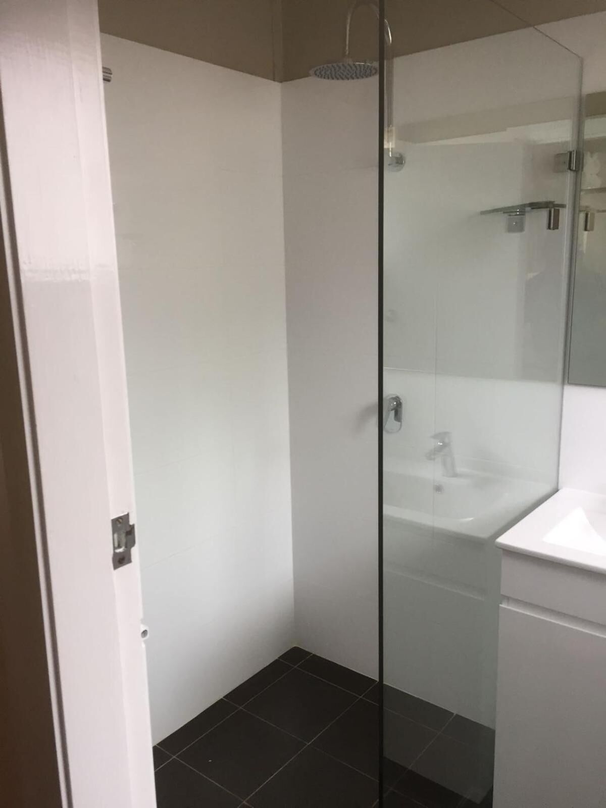 Un baño moderno con mampara de vidrio, lavabo blanco y suelo de baldosas oscuras.
