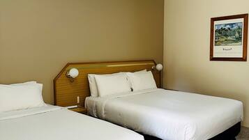 A hotel room with two beds, a wooden headboard, a framed picture on the wall, and a carpeted floor.