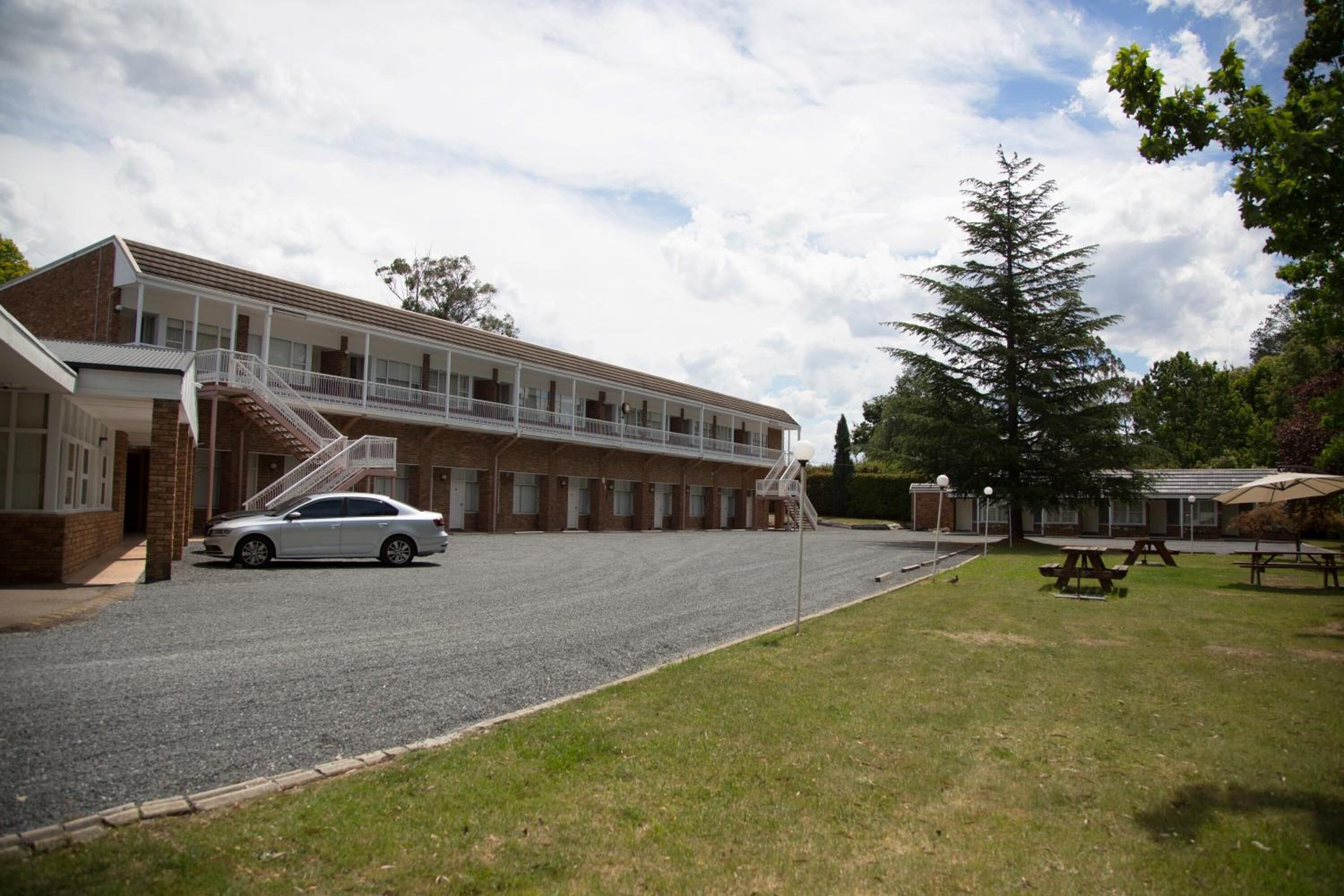 A two-story motel with a covered parking area, a staircase leading to the upper floor, and picnic tables in the yard.