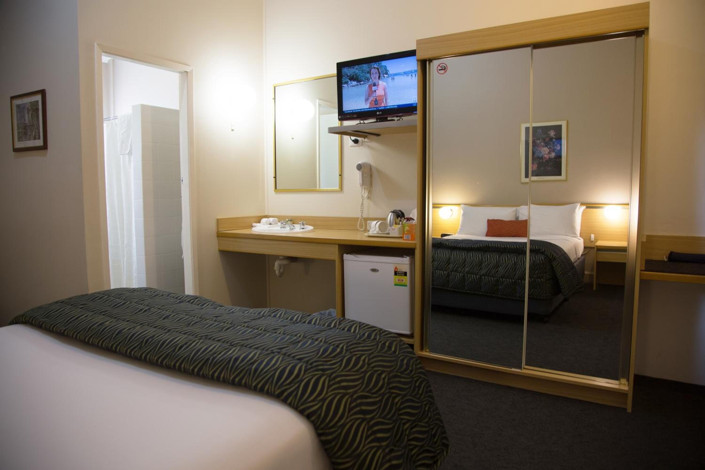 A hotel room with a bed, a desk with a mirror, a television, and a small refrigerator.