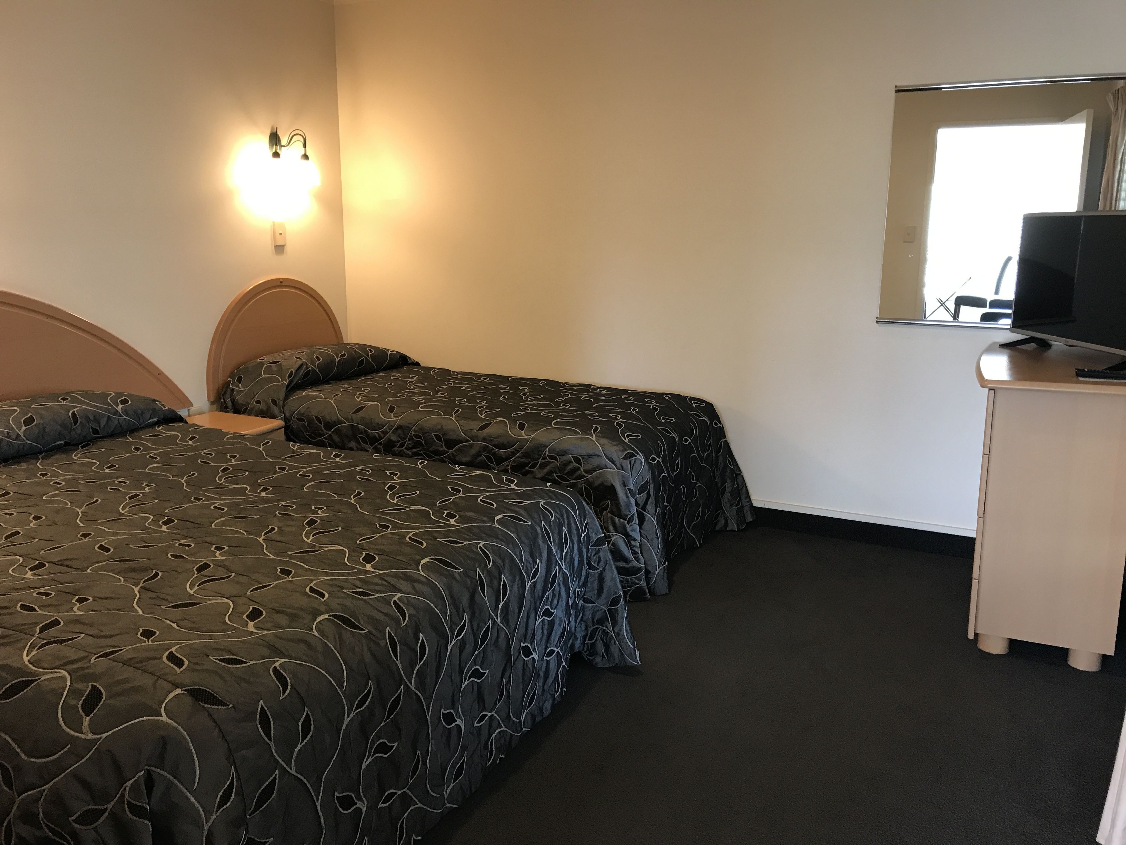A hotel room with two single beds, a desk with a television, and a window with a view.