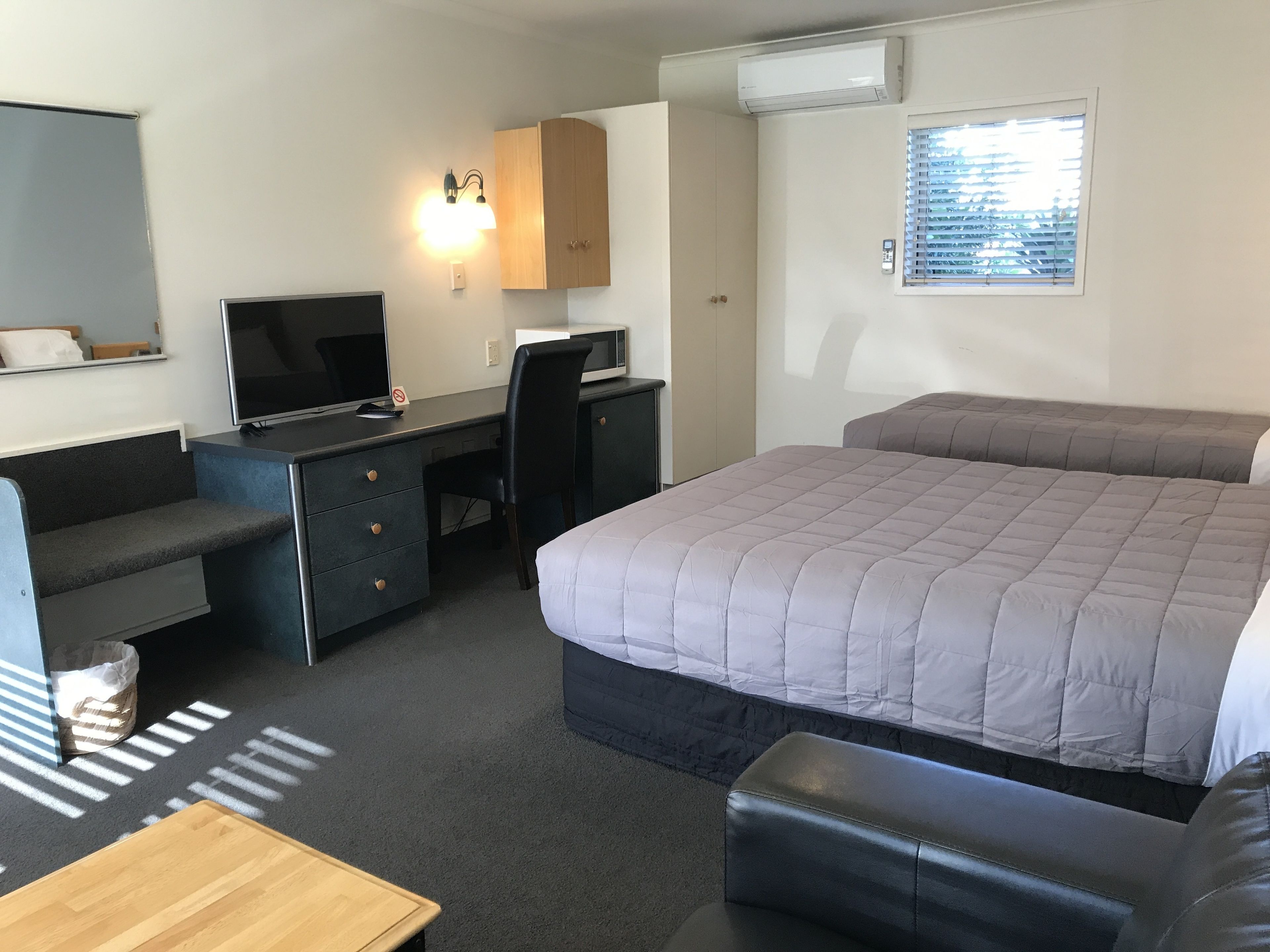 A hotel room with a bed, a desk with a computer, a TV, and a window with blinds.