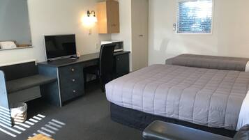 A hotel room with a bed, a desk with a computer, a TV, and a window with blinds.
