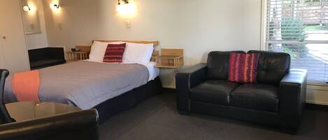Habitación de hotel con cama, sofá de cuero negro, una mesita y ventana con persianas.