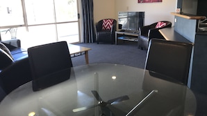 Un salon moderne avec une table en verre, des fauteuils en cuir noir, un téléviseur à écran plat et un tableau accroché au mur.