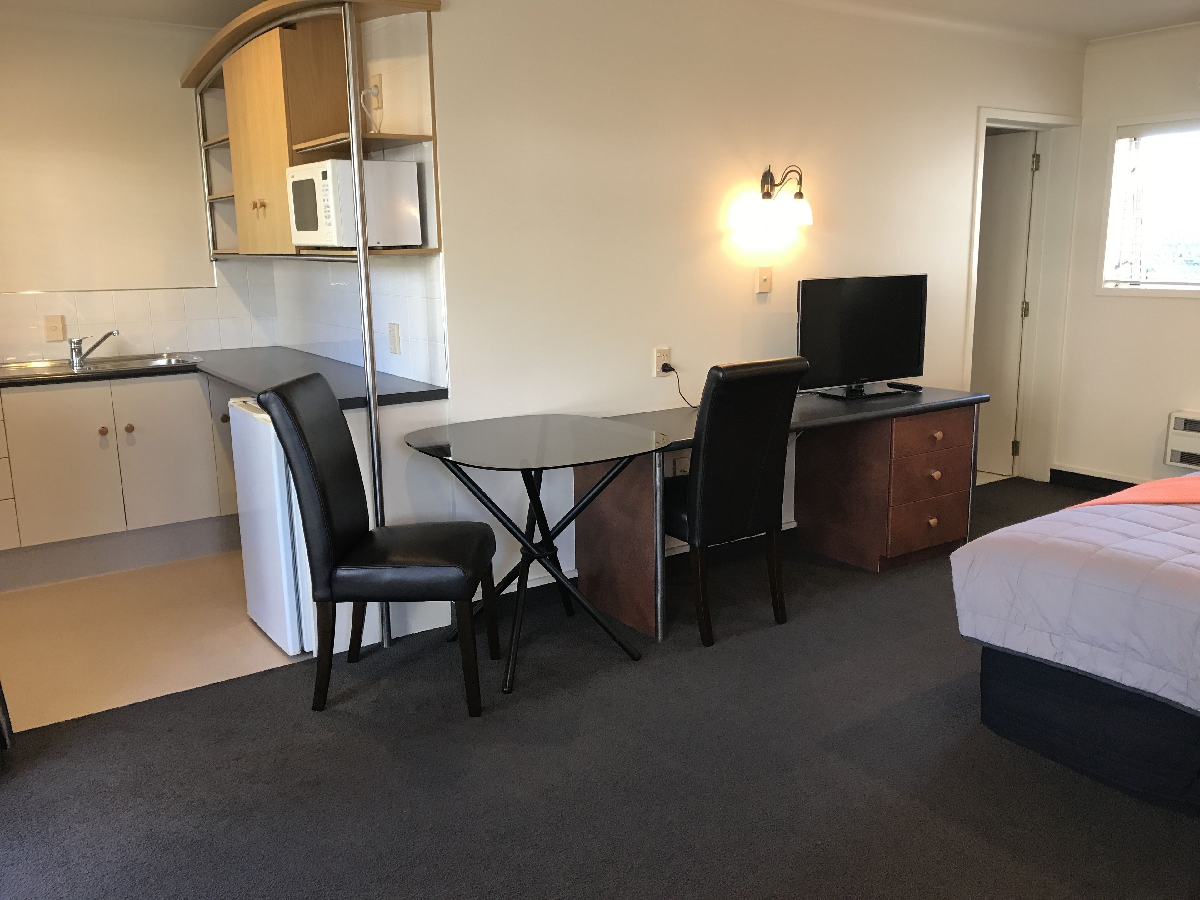 A compact hotel room with a kitchenette, a small dining table with two chairs, a TV, and a bed.