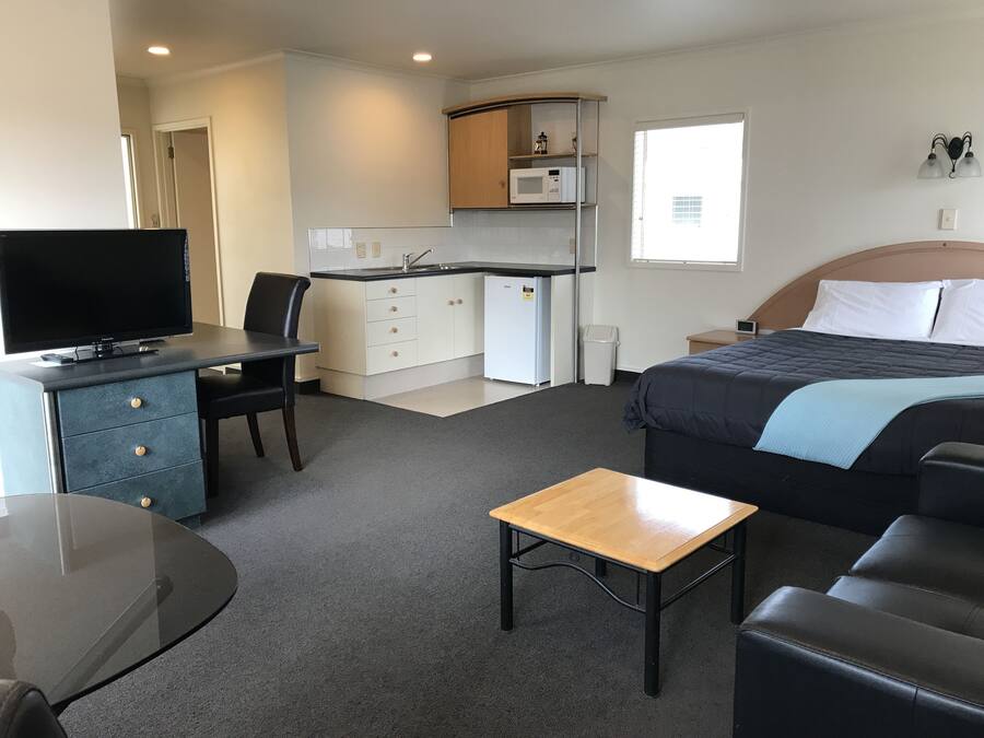 Een compacte hotelkamer met een bed, een bureau met een televisie, een kleine kitchenette en een zithoek.