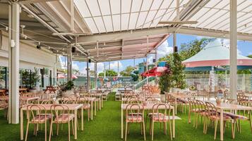 An outdoor dining area with tables and chairs, a covered section with a roof, and a green artificial turf floor.