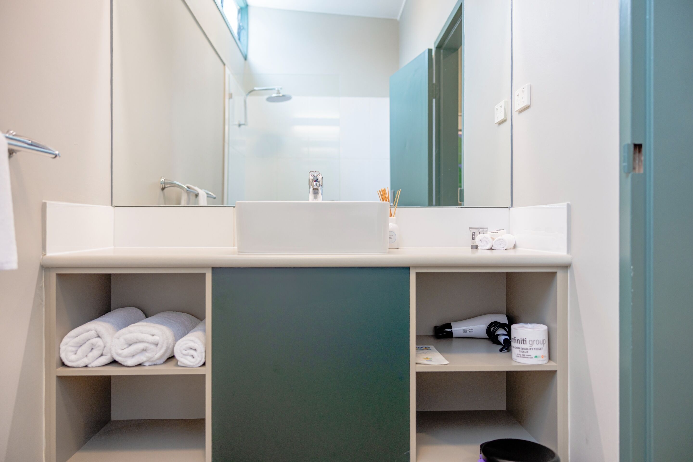 Een moderne badkamer met een grote spiegel, een wastafel en planken met handdoeken en toiletartikelen.
